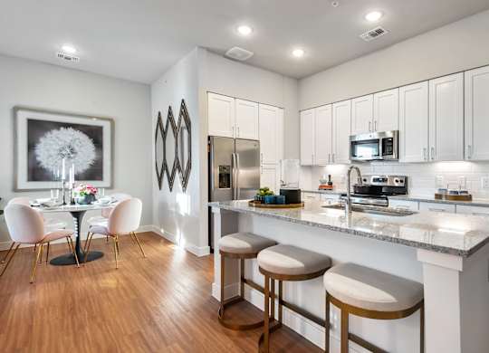 A kitchen with white cabinets and a bar area with stools.