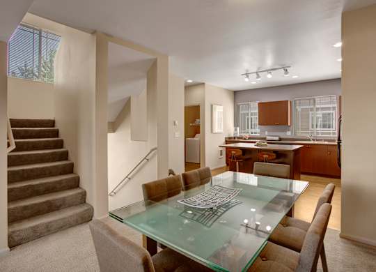 A glass dining table with brown chairs in a room with a staircase.