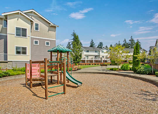 A playground with a green slide and a red swing set in front of apartment buildings.