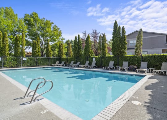 a swimming pool with lounge chairs and trees in the background