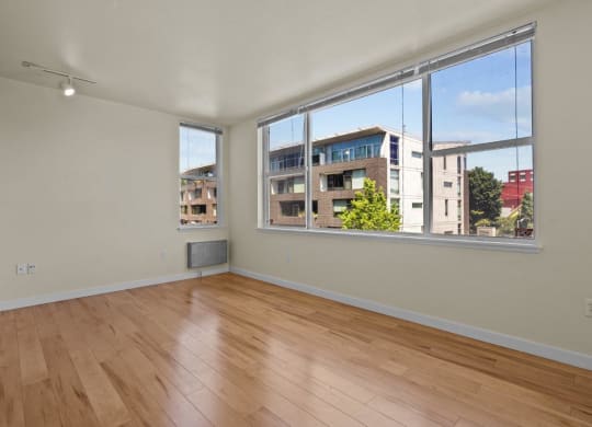 Living room with large windows, wood-style flooring, and white walls at Collins Circle apartments in the Goose Hollow district in Portland, Oregon.
