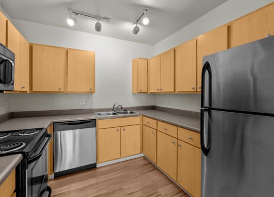 Kitchen with stainless steel appliances, wooden-style flooring, and overhead lighting at Collins Circle apartments in the Goose Hollow district in Portland, Oregon.