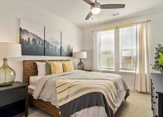 A bedroom with a bed, a ceiling fan, and a painting on the wall.
