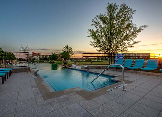 A pool surrounded by blue lounge chairs and a tree. at Discovery at The Realm, Texas