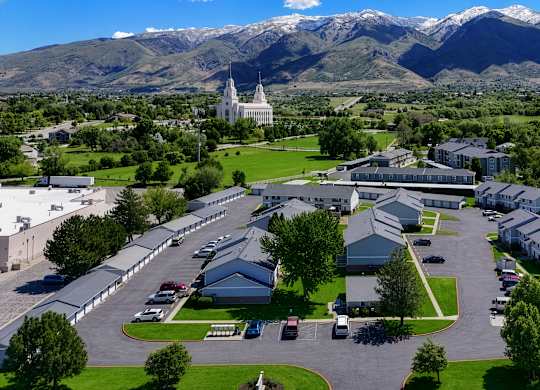 A large white building with a green lawn in front and mountains in the background.