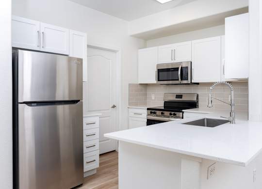 A kitchen with a stainless steel refrigerator, white countertops, and white cabinets.