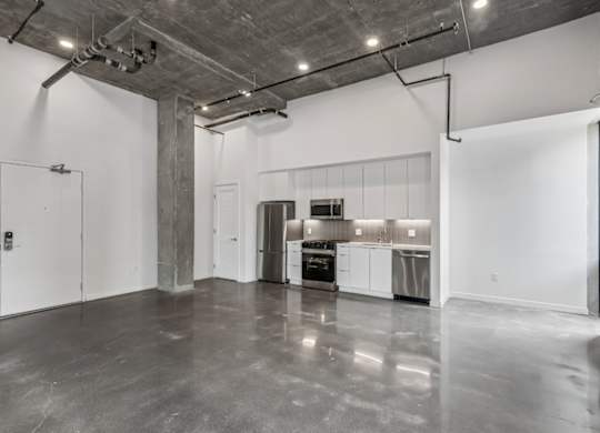 A large empty room with a kitchen area in the background.