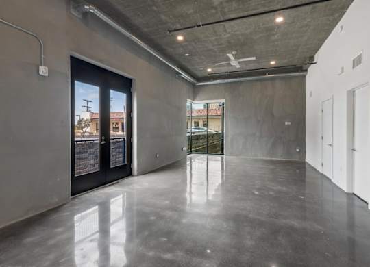 A spacious room with a concrete floor and walls, featuring a large window with a view of the outside.