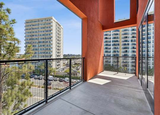A balcony with a black railing and a view of a parking lot and a building.