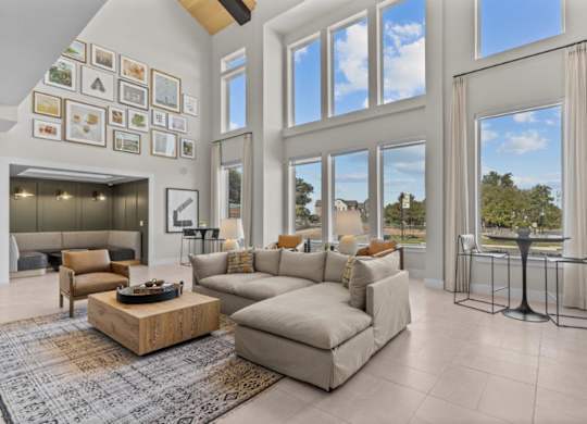 A living room with a large couch, a coffee table, and a view of the trees outside the windows.