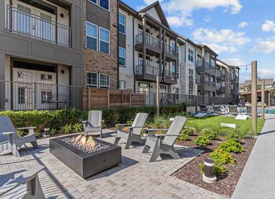 A modern outdoor seating area with a fire pit in the middle of a brick patio.