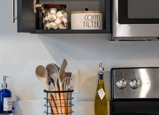 A kitchen with a stove, a microwave, and a container of coffee filters.