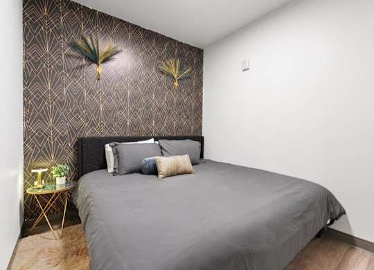 A bedroom with a grey bed and a wallpapered wall.