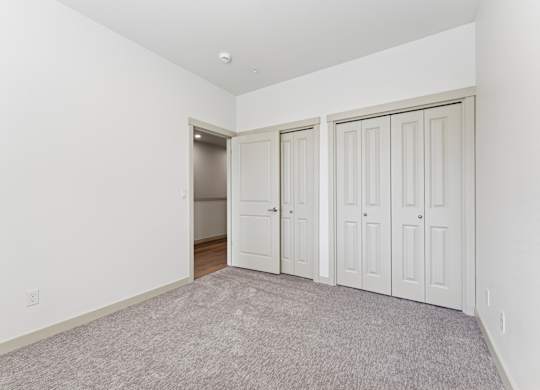 A room with white walls and a carpeted floor with three doors.