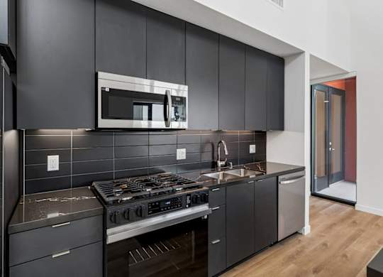 A modern kitchen with dark grey cabinets and a stainless steel stove top.