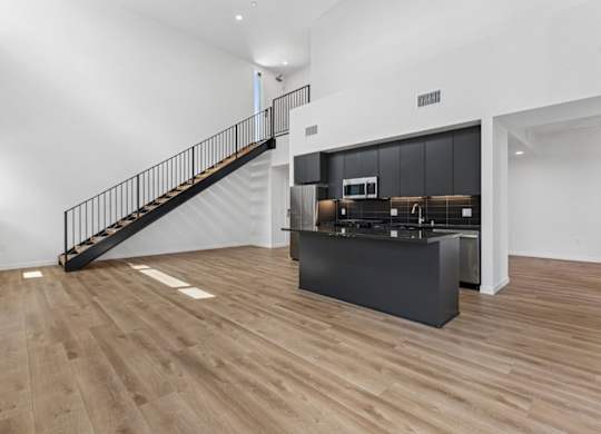 A black staircase with a metal railing leads to a kitchen area.