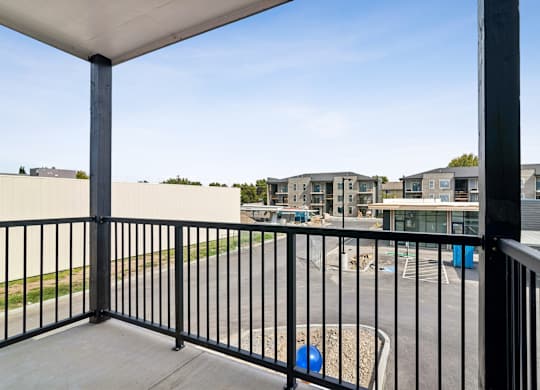 A balcony with a black railing overlooks a parking lot and buildings.