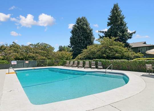A large outdoor swimming pool surrounded by trees and a fence.