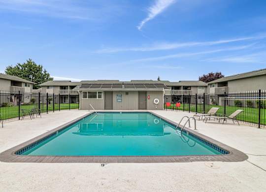 A swimming pool surrounded by a black fence and a building in the background.