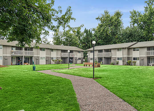 A grassy area with a concrete walkway separates the front of apartment buildings.