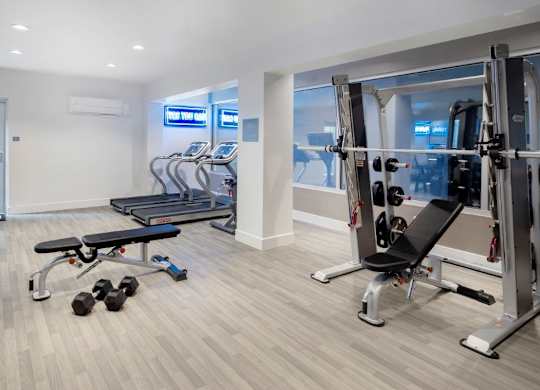 A gym with a variety of equipment including dumbbells, a bench, and a leg press machine.