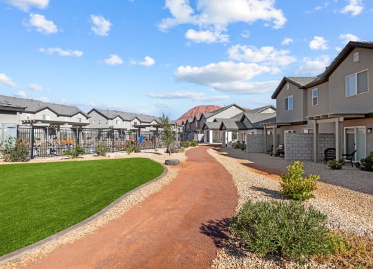 a pathway leading to a row of houses with a field of green grass and