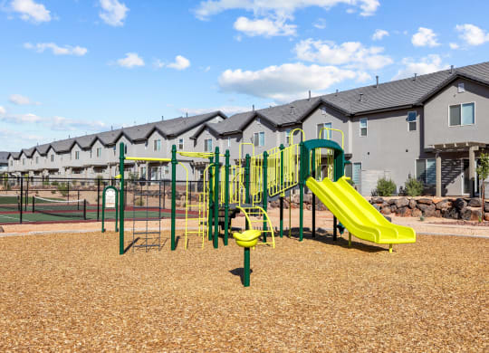 a playground with yellow and green equipment in front of apartments