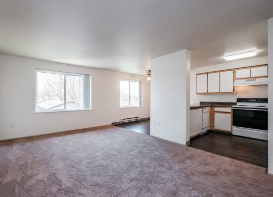 an empty living room with a kitchen in the background
