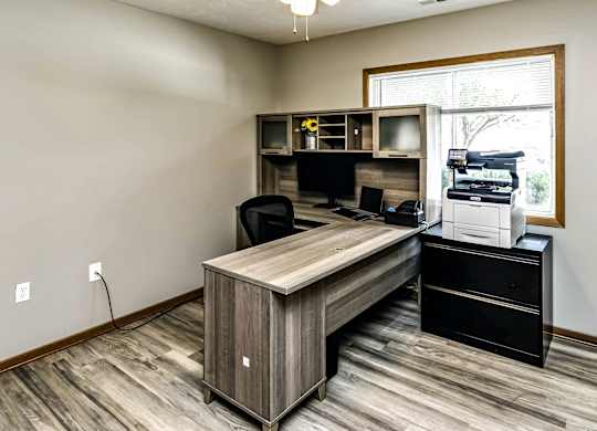 A room with a desk, chair, and a printer on a cabinet.