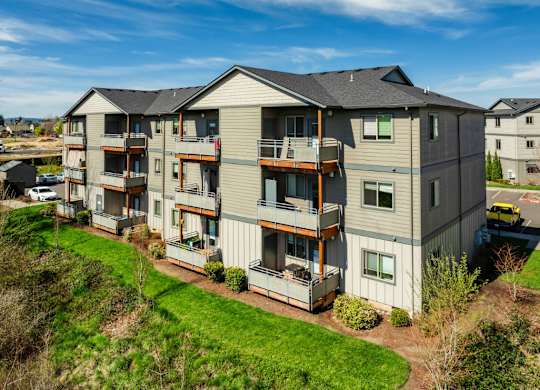 A large apartment building with multiple balconies and a green lawn in front.