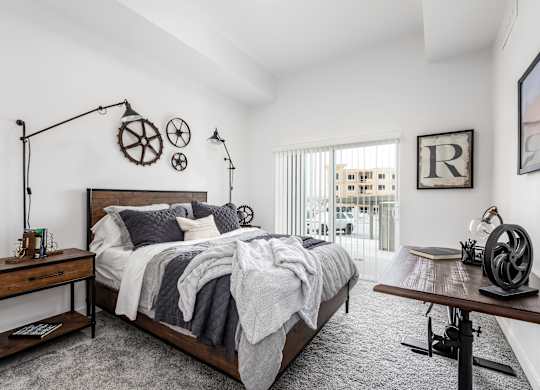 A bedroom with a large bed, a wooden table, and a window with a view of a building outside.
