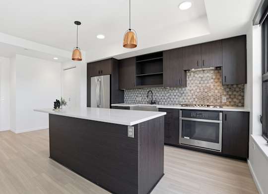 A modern kitchen with a dark island and wooden floors.