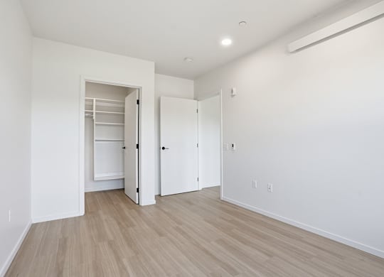 A room with a white wall and a wooden floor with a white door and a white closet.