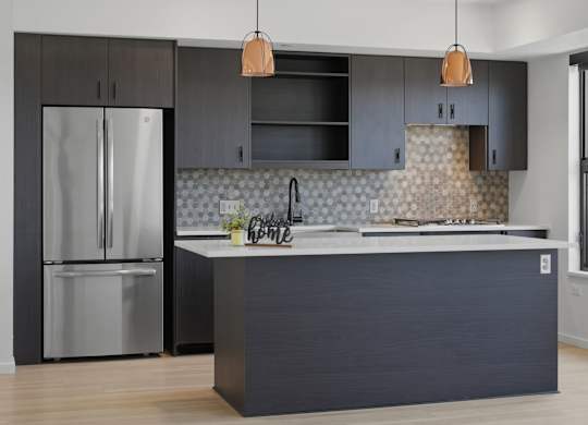 A modern kitchen with a dark grey island and a stainless steel refrigerator.