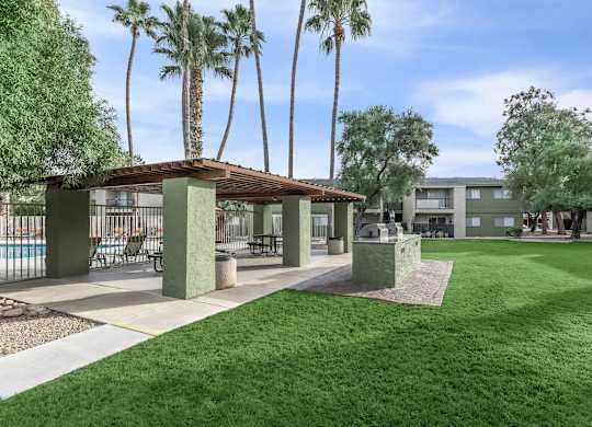 A sunny day at the poolside with palm trees and a covered seating area.