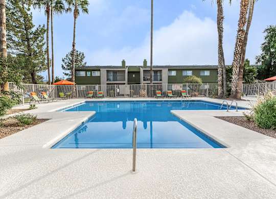A swimming pool surrounded by palm trees and a building in the background.
