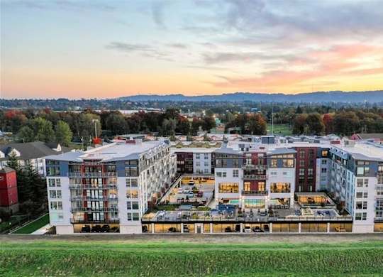 A large, modern apartment complex with a green field in the foreground and a cityscape in the background.
