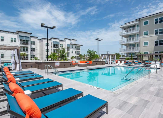 a swimming pool with blue chaise lounge chairs and an apartment building in the background