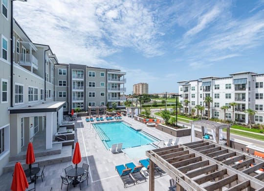 a swimming pool with lounge chairs and umbrellas in front of an apartment building