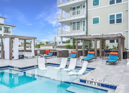 a swimming pool with chairs and a building in the background