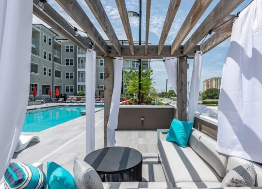 a pergola with blue and white pillows on a patio next to a pool