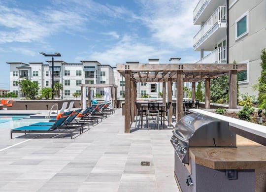 a patio with a grill and lounge chairs next to a swimming pool