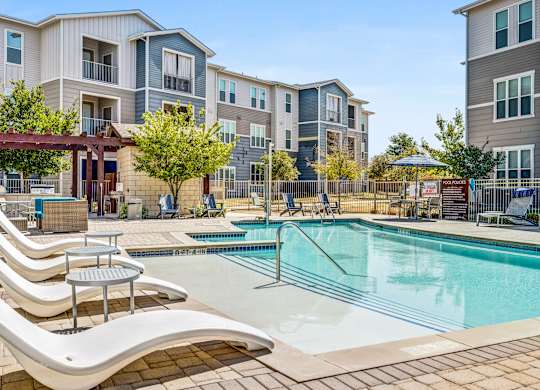 A pool area with sun loungers and a building in the background.