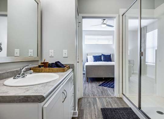 A bathroom with a sink, mirror, and a bedroom in the background.