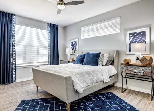 A bedroom with a bed, a ceiling fan, and a window with blue curtains.