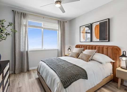 A bedroom with a large bed, a ceiling fan, and a window with a view of the sky.