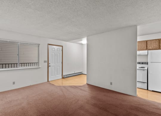 the living room and kitchen of an apartment with white appliances and wood flooring