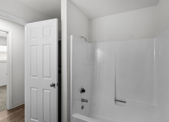 an empty bathroom with a white shower and a white door