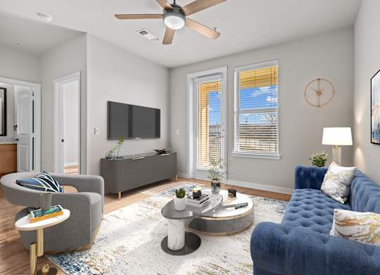A living room with a grey sofa, a grey armchair, a coffee table, a ceiling fan, and a flat screen TV.