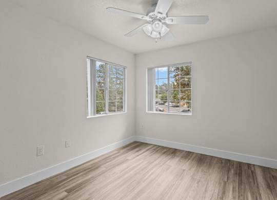A room with a ceiling fan and two windows.
